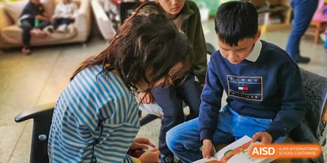 A close-up of a student and teacher leaning over a table, reading a book together in a class at Kunming International Academy.
