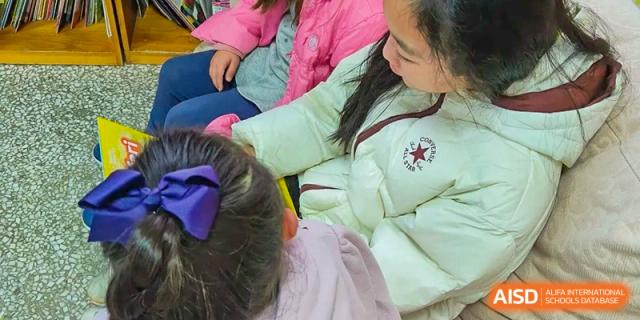 A student with a purple bow in her hair learning or receiving help from a teacher in a classroom at Kunming International Academy.