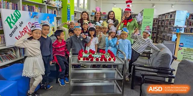 A large group of young students and teachers posing for a picture with a tiered display of red roses or cupcakes at an event at Kunming International Academy.