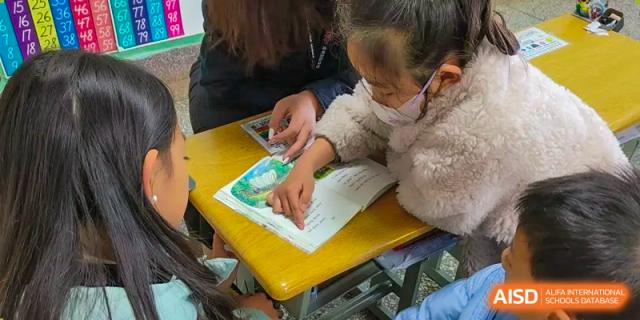 A young student wearing a face mask pointing at a book while working with a teacher or parent at a small desk at Kunming International Academy.