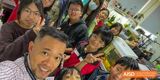 A close-up selfie of a diverse group of students and adults smiling and posing for the camera at a Kunming International Academy event.