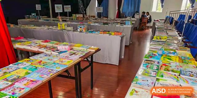 A wide shot of tables covered with books and learning materials set up for a book fair or resource event at Kunming International Academy.