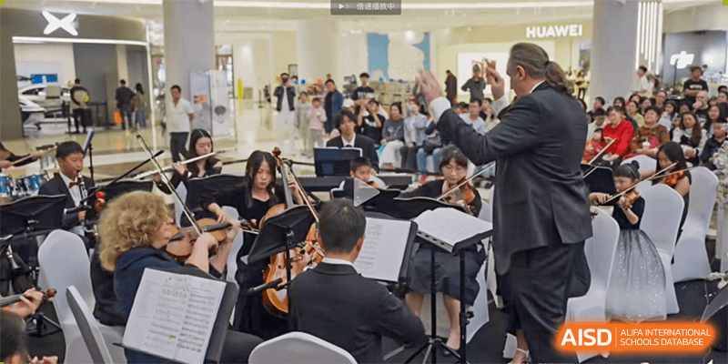 Students playing instruments as part of an orchestra or musical ensemble with a conductor visible at Kunming International Academy.