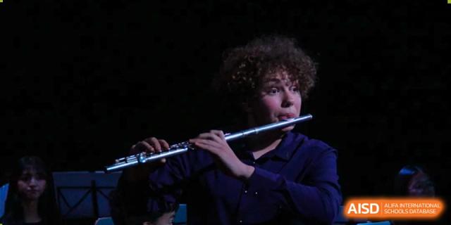 A student with curly hair playing the flute in a dimly lit setting during a musical performance at Kunming International Academy.