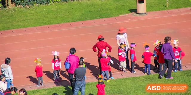 Young children in bright clothing playing a game or running on a red outdoor track at Kunming International Academy.