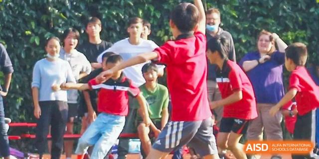 A student in a red shirt throwing a ball or participating in a sports activity, surrounded by spectators at Kunming International Academy.