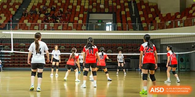 A female student volleyball player on the court, ready to receive a serve during a match in the school gymnasium at Kunming International Academy.