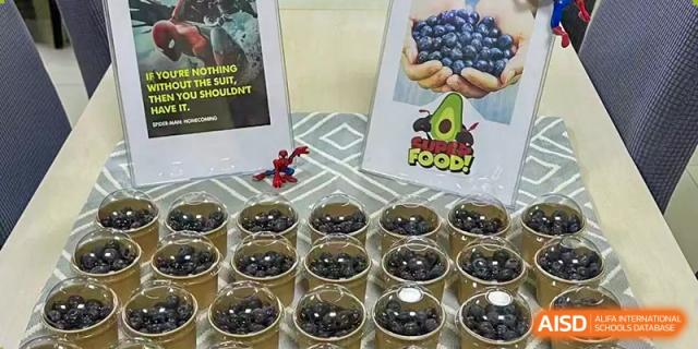 A display table with cups of fresh blueberries and avocado-themed branding at a school market event at Kunming International Academy.