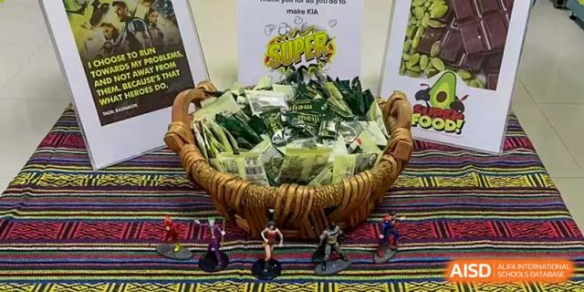 A large basket filled with packaged snacks, small figurines, and a promotional sign at a school market or fair at Kunming International Academy.