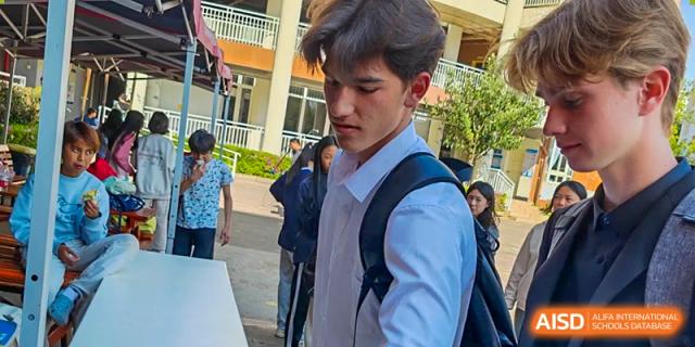A portrait of a male student with a backpack slung over his shoulder, standing outdoors at Kunming International Academy.