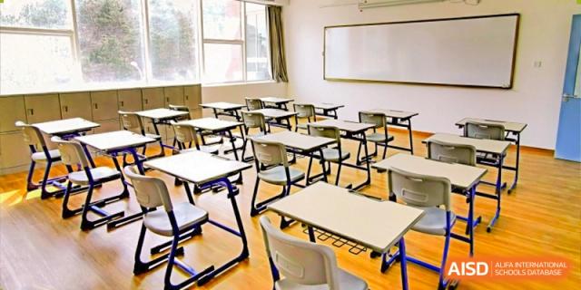 A bright, empty traditional classroom at Milton International School Qingdao featuring rows of individual desks and a large whiteboard.