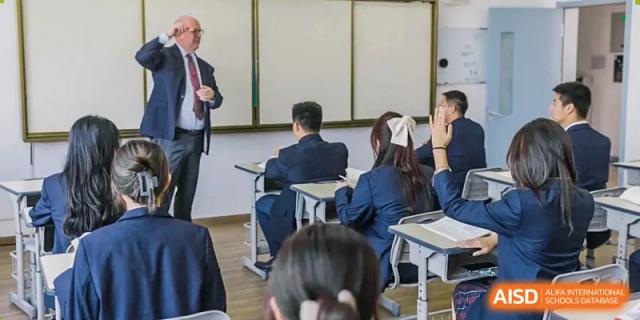 A teacher or guest speaker addressing a class of students from Milton International School Qingdao, who are seated at their desks in their school uniforms.