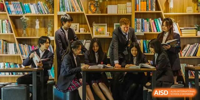 A teacher and a group of students from Milton International School Qingdao gathered around a table, reviewing documents in the school's library among bookshelves.