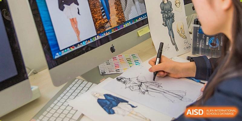 Fashion design student sketching with a pen, surrounded by digital art on a desktop computer at Milton International School Qingdao.