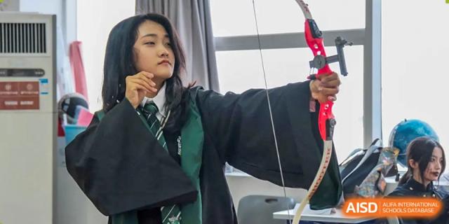 Female student in uniform practicing archery with a bow and arrow at Milton International School Qingdao.