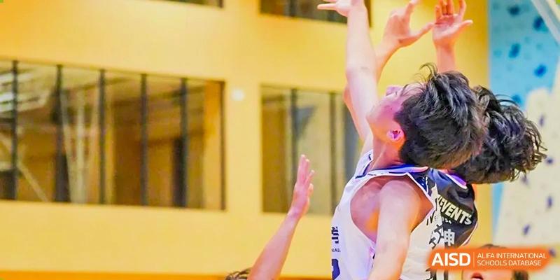 Student reaching for the basketball during a game in the indoor court at Milton International School Qingdao.