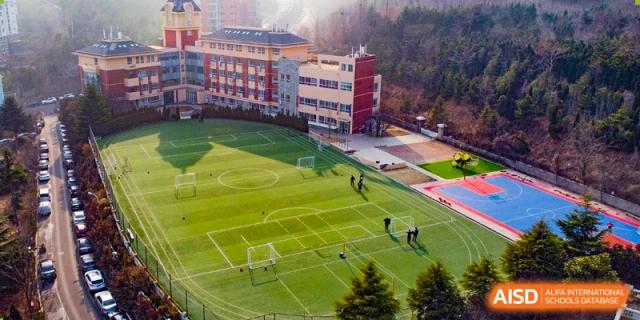 Aerial view of the large school campus and sports field on a sunny day at Milton International School Qingdao.