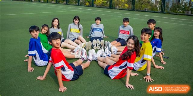 Milton International School Qingdao students relaxing together outdoors on a green sports field, wearing casual and school-related apparel.