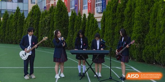 Female students from Milton International School Qingdao in school uniform performing music outdoors with a keyboard and microphone.