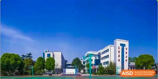 A view of the modern, white academic buildings of Milton International School Qingdao with a bright blue outdoor basketball court in the foreground.