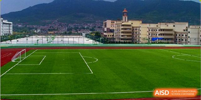 The large, pristine green artificial turf sports field and track at Milton International School Qingdao, with a traditional school building visible in the background.