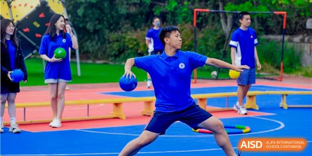 A student from Milton International School Qingdao in a blue sports uniform playing a game on a blue court, mid-throw.