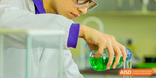 A group of Nanjing International School students in lab coats and goggles performing a science experiment together.