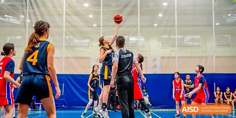 Nanjing International School girls' basketball player reaching for a layup against an opponent with a referee watching closely.