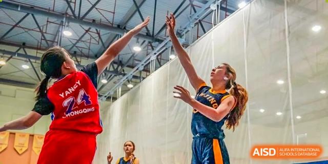 A close-up action shot of a Nanjing International School girls' basketball player shooting or defending with arms raised high.