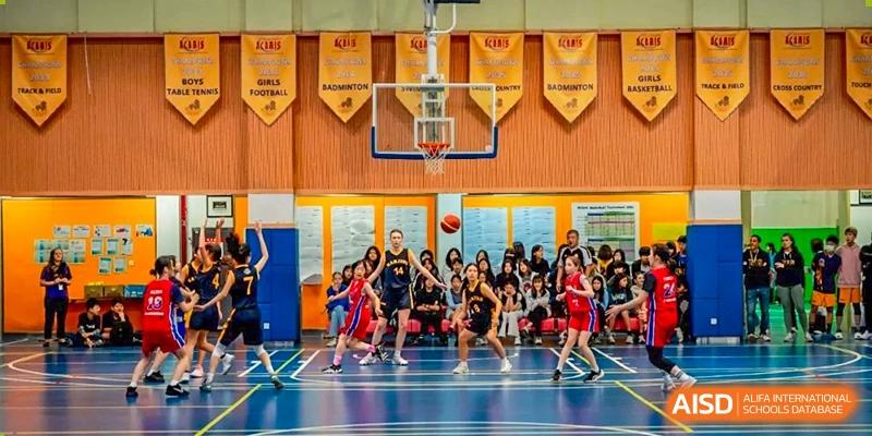 A wide shot of a Nanjing International School basketball game with many students watching from the sidelines.