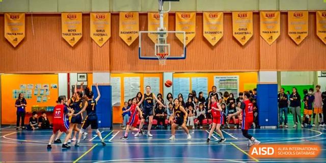 A wide shot of a Nanjing International School basketball game with many students watching from the sidelines.