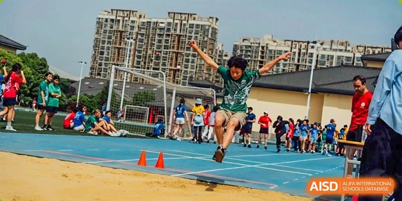 A group of Nanjing International School students running on a blue track during a race, with buildings in the background.