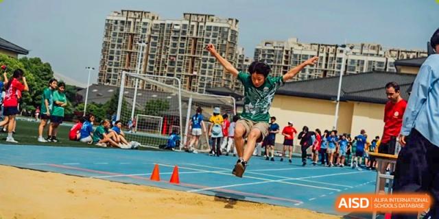 A group of Nanjing International School students running on a blue track during a race, with buildings in the background.