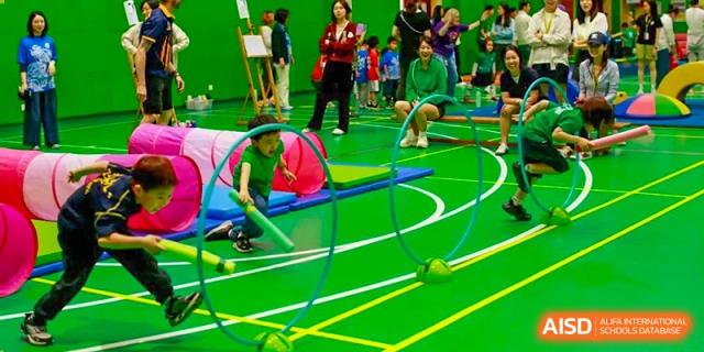 A group of young Nanjing International School students participating in an indoor sports carnival, crawling through a tunnel and using hoops.