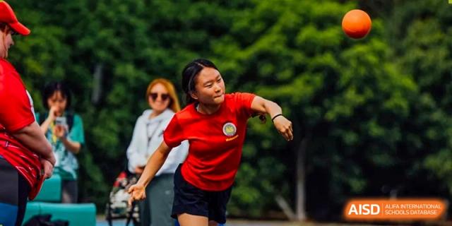 A Nanjing International School student-athlete in a red shirt throwing a shot put or discus during a track and field competition.
