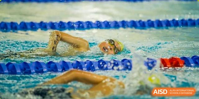 A Nanjing International School swimmer in a yellow cap doing the freestyle stroke in an indoor pool.