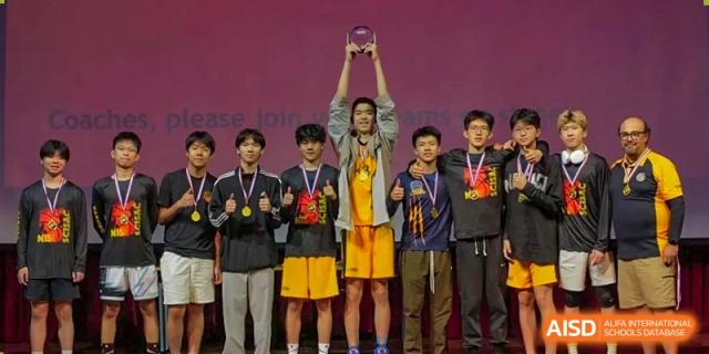 Nanjing International School male athletes on a podium, holding medals and a trophy after winning a sports championship.