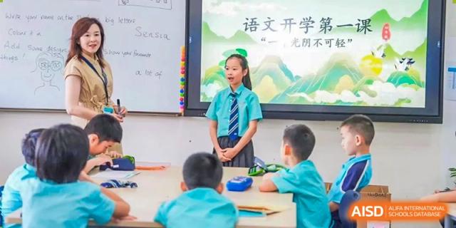 A Nord Anglia Chinese International School Shanghai student in a school uniform standing and presenting to classmates who are working at tables.