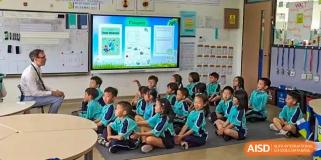 A group of Nord Anglia Chinese International School Shanghai students sitting on the floor, attentively looking at a large digital screen in the classroom.