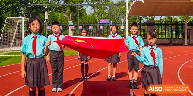 Three Nord Anglia Chinese International School Shanghai students in uniform holding a large Chinese flag on an outdoor track.