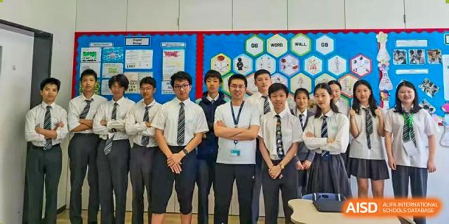 A group of older Nord Anglia Chinese International School Shanghai students and male teachers posing together in front of a colorful classroom display wall.