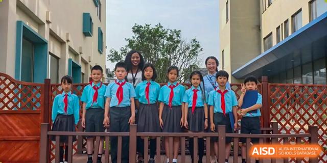 A female teacher and a group of young Nord Anglia Chinese International School Shanghai students in uniforms posing together outdoors on a balcony or steps.