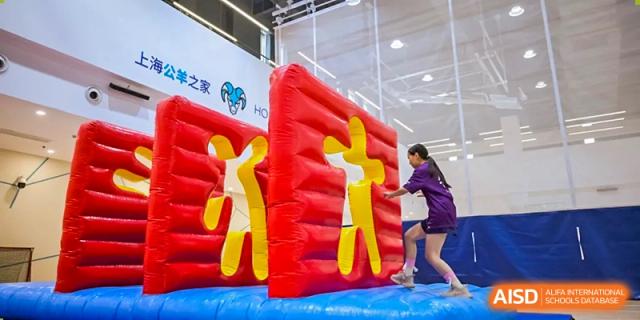 Nord Anglia Chinese International School Shanghai students navigating a large, red and yellow inflatable obstacle course indoors.