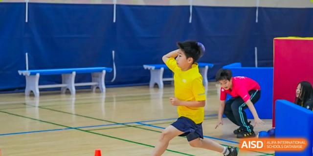 A Nord Anglia Chinese International School Shanghai student in a yellow shirt running quickly during an indoor sports activity.