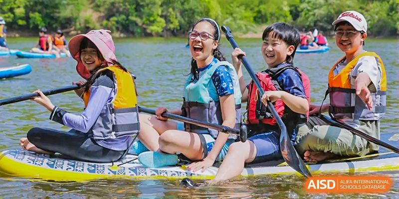 Nord Anglia Chinese International School Shanghai students smiling while sitting on a stand-up paddleboard in a lake, wearing life vests.