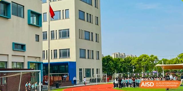 The exterior of a modern, multi-story building at Nord Anglia Chinese International School Shanghai with a track and field area visible in the foreground.