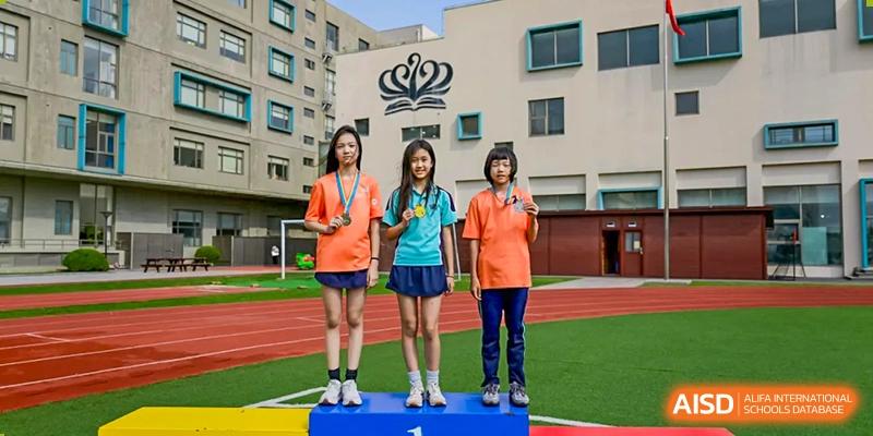 Three Nord Anglia Chinese International School Shanghai students in sports uniforms standing on a winner's podium on an outdoor field.
