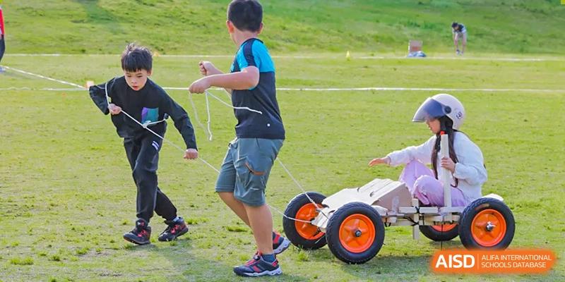 A Nord Anglia Chinese International School Shanghai student pulling a small, wheeled cart during an outdoor school activity or race.