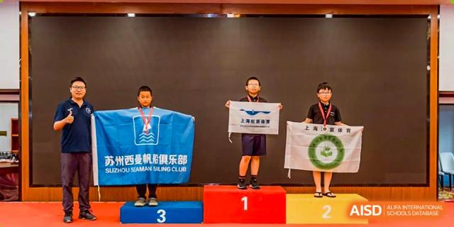 Two Nord Anglia Chinese International School Shanghai students standing on a first and second-place podium holding a banner after a competition.