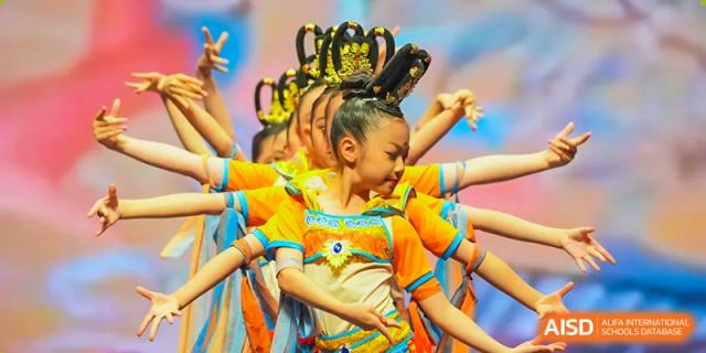 Close-up of Nord Anglia Chinese International School Shanghai students performing a vibrant traditional dance in bright yellow and orange costumes and elaborate headpieces.